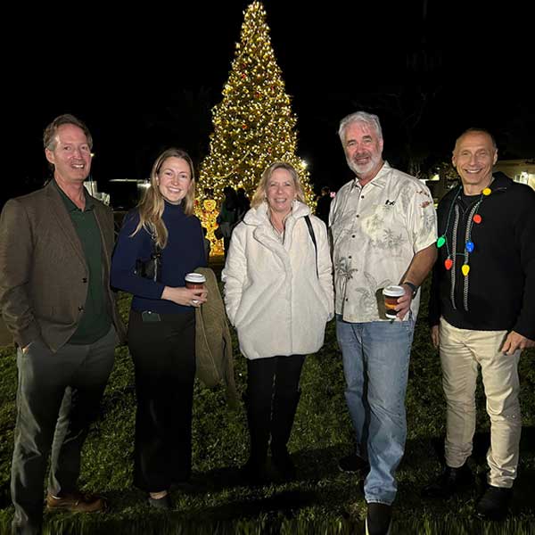 group of men and woman standing in front of christmas tree