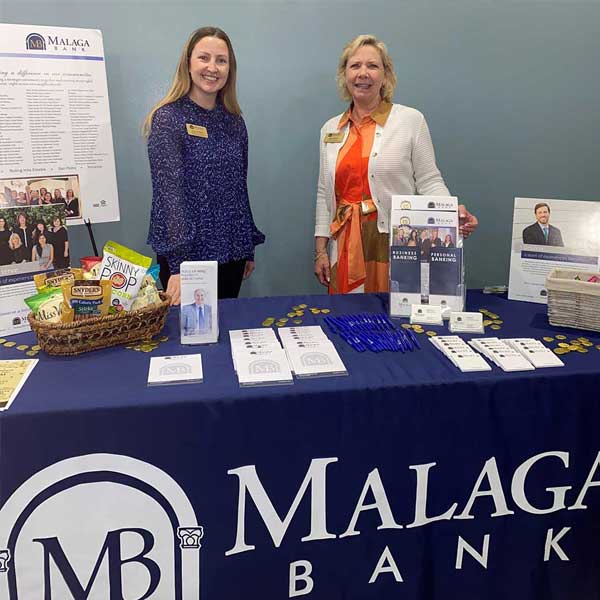 Two women standing behind a desk at a tradeshow